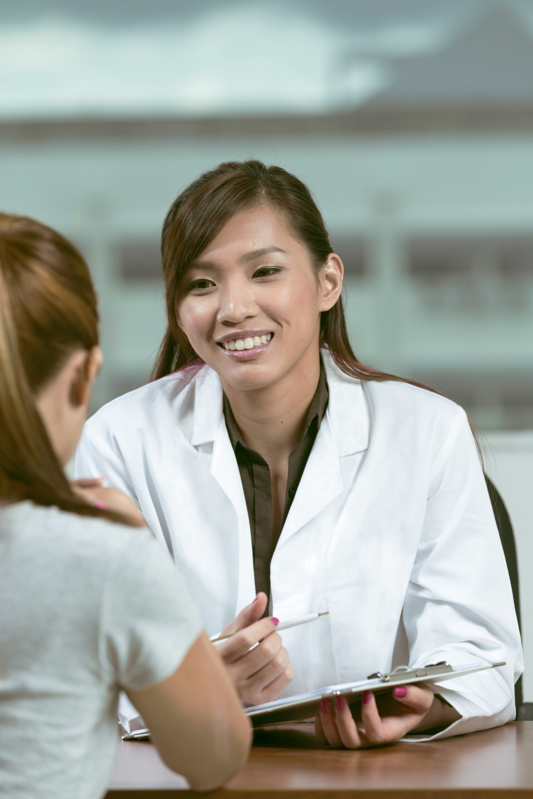 Chinese doctor talking with female patient in doctors office.